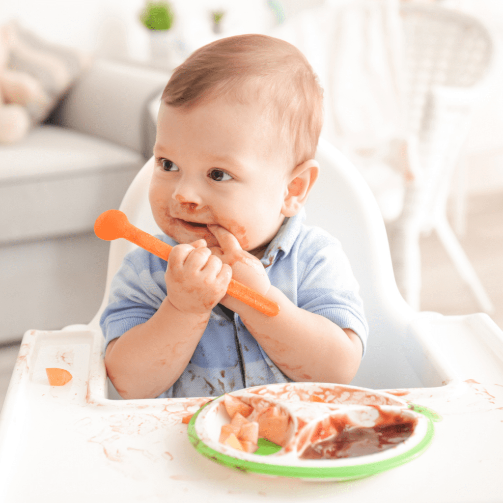 Main image for the article [How to manage food throwing at the table]. Pictured is a baby eating his highchair and making a mess with his food.