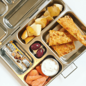 Main image for the article [How a simple mindset shift can remove the stress from lunch packing]. Pictured is lunchbox with homemade pizza, carrots and dip, olives, pears and a granola bar.