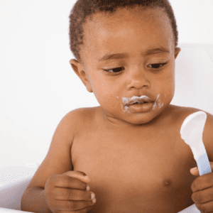 Child sitting in a high chair holding a baby spoon