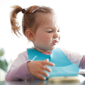 Main image for the article [Avoiding Food Ruts With The “Rotation Rule” ]. Pictured is a toddler sitting at the table and making a disgusted face at her food. 