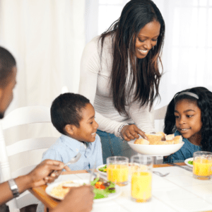 Main image for the article [Why And How To Start Serving Family Style Meals]. Pictured is a family eating salad and rolls together. 