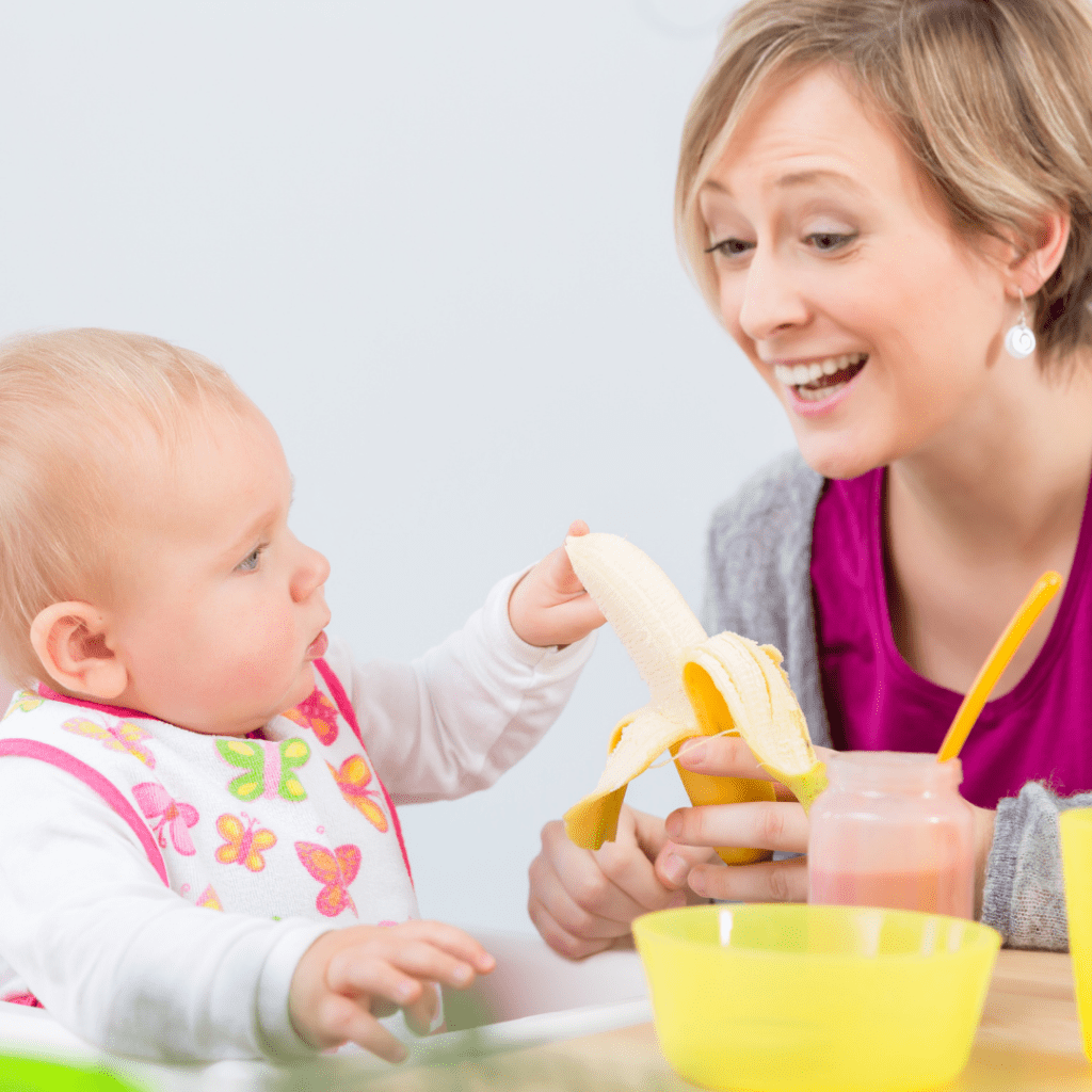 Episode art for episode “#11: My Top 8 Foods for Starting Solids”. Pictured is a baby sitting in a highchair, and a woman feeding the baby a whole, peeled banana.