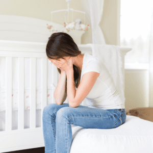 Main image for the article [Mom Shame and How to Eliminate Societal Pressures to be the Perfect Mom]. Pictured is an upset mother resting her face in her hands.