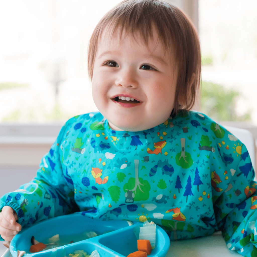 Main image for the article [What is toddler led feeding?]. Pictured is a baby sitting in a highchair, eating carrots with a fork.