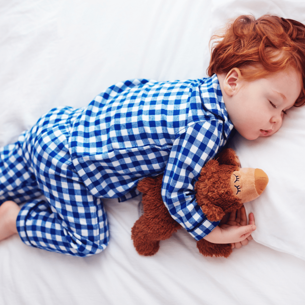 Main image for the article "Common Toddler Sleep Problems and How You Can Manage Them". Pictured is a sleeping toddler cuddling their teddy bear.