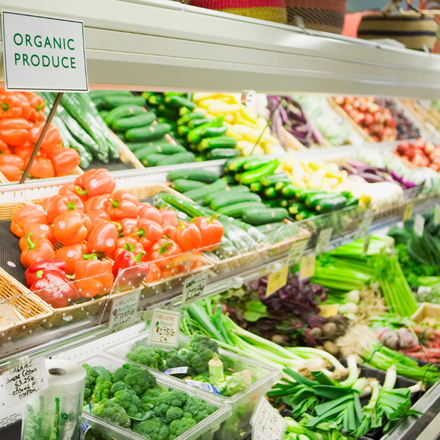 Episode art for episode: “#54 ORGANIC FOOD for Babies - What You NEED to Know and WHAT IT SAYS ABOUT YOU as a Parent”. Pictured is a supermarket with an organic produce sign above tomatoes, zucchini, broccoli, and other vegetables. 