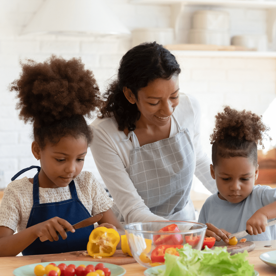 A mother and her two kids in the kitchen cutting vegetables